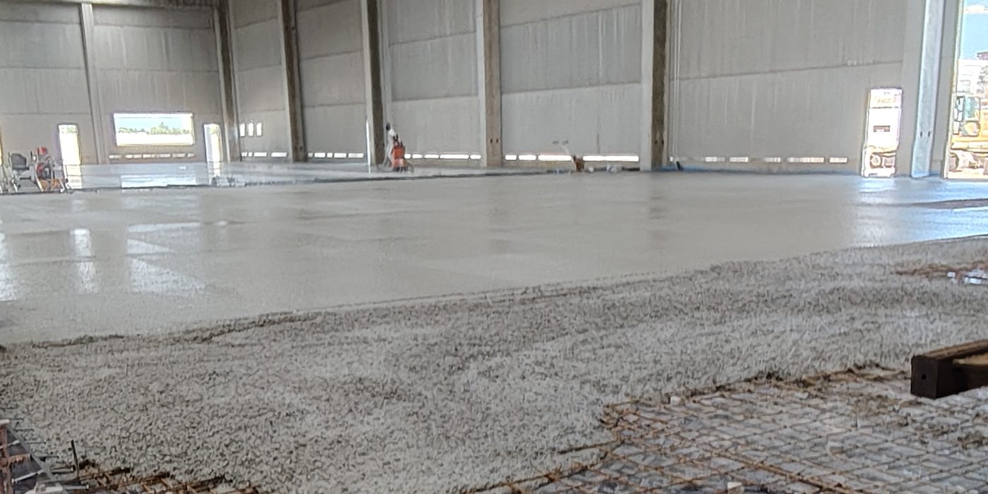 Capannone con pavimentazione industriale in calcestruzzo appena gettata e rete di armatura in primo piano