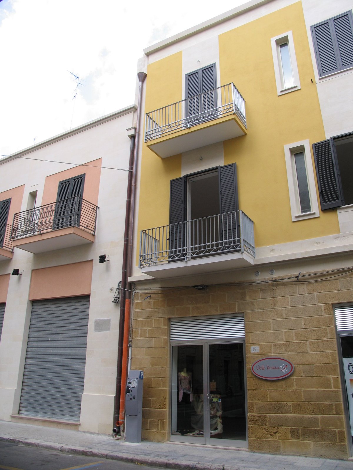 Edificio residenziale a Lecce ristrutturato, con negozi al piano terra: facciata a tre piani con campiture gialle e bianche, balconi con ringhiera in ferro e piano terra in conci di pietra