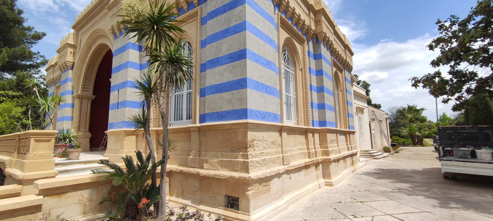 Villa Arabesca dopo il restauro: angolo del prospetto con fasce orizzontali blu e ocra, portale ad arco e palme